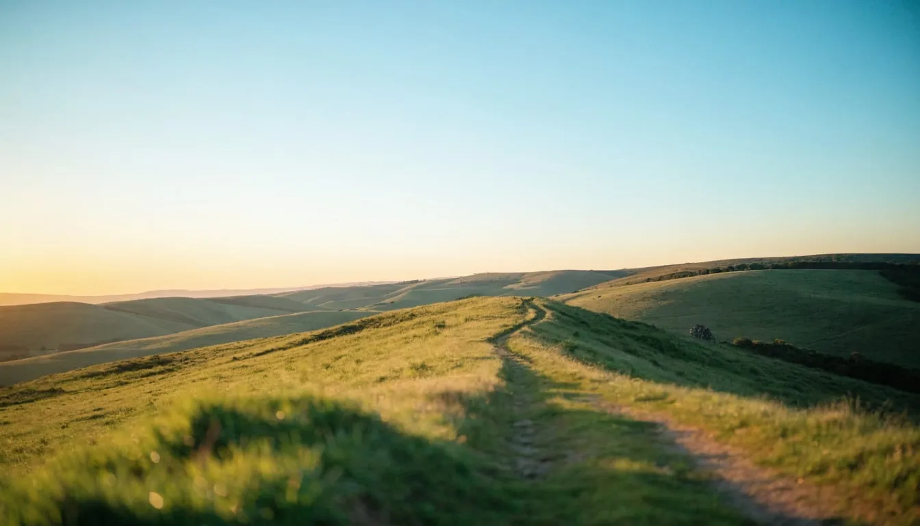 Sunrise over rolling green hills with a winding footpath toward the horizon