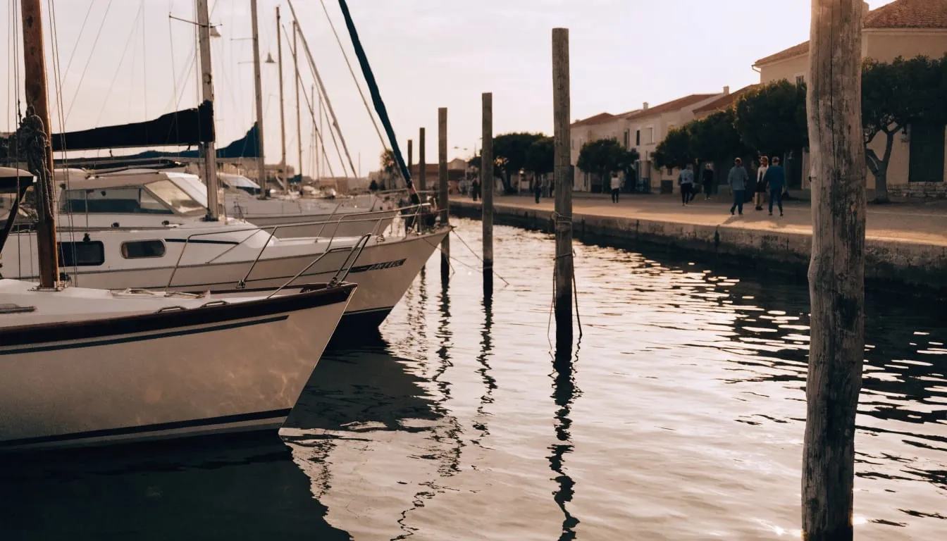 Sailboats in a small marina at golden hour with people strolling the waterfront
