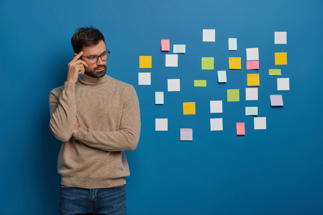 Someone stands deep in thought beside a blue wall covered in scattered sticky notes.